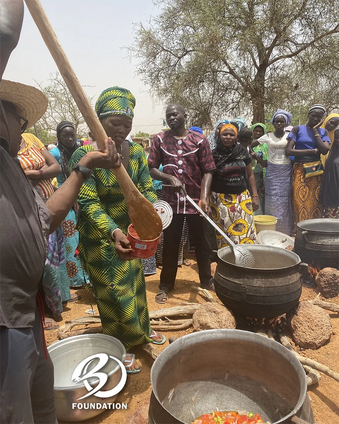 Women and community members gathered around cooking pots during a visit in Kaya.